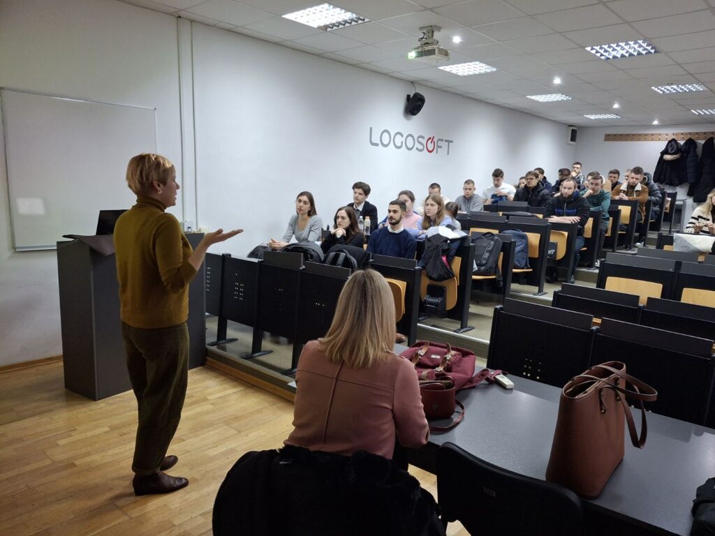 Studenti u prilično punoj predavaonici slušaju, predavačica predaje, projekcija na platnu